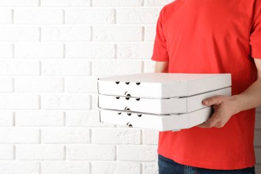 Pizza kutuları yakınındaki beyaz tuğla duvar, metin için yer olan genç adam. Gıda dağıtım hizmeti