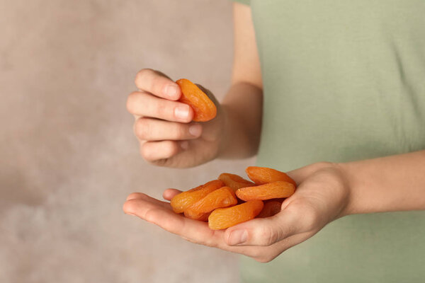 Woman holding handful of dried apricots on color background, space for text. Healthy fruit