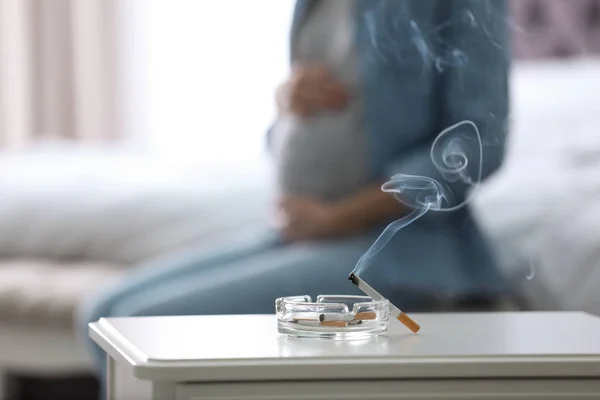 烟灰缸里的香烟和模糊的孕妇在背景上 特写镜头 文本的空间 — 图库照片