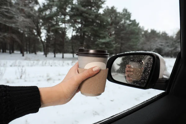 Young woman with coffee in car among winter forest, closeup