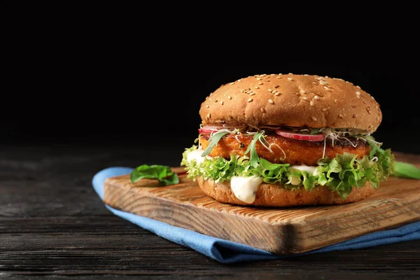 Board with tasty vegetarian burger on wooden table