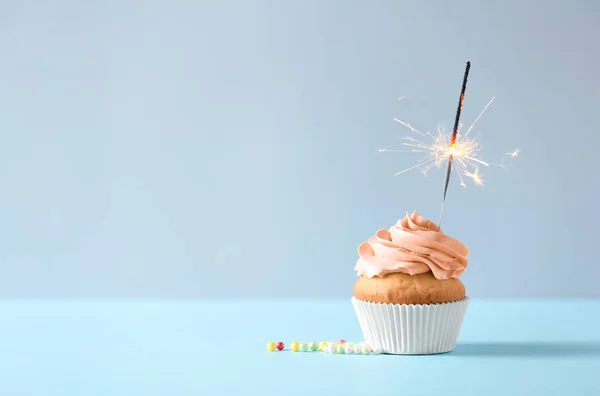 Delicious orange cupcake with burning sparkler on table against light background. Space for text