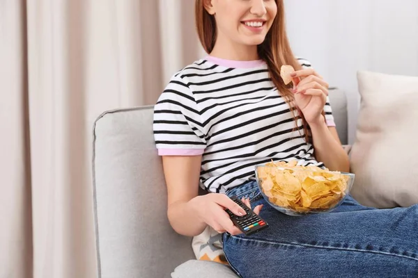 Woman with bowl of chips on couch, closeup. Watching TV