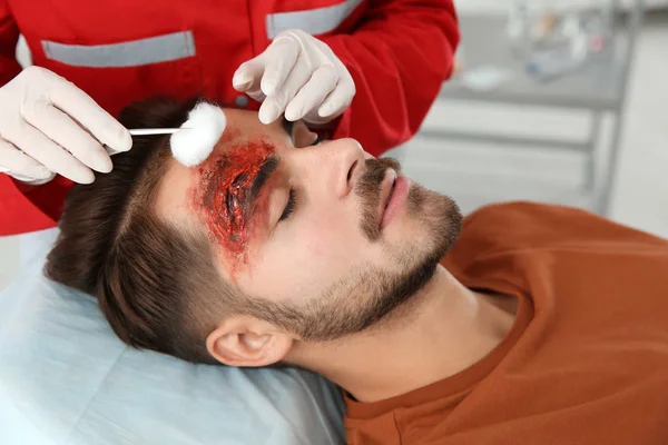 Nurse cleaning young man\'s head injury in clinic. First aid