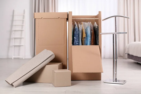 Cardboard wardrobe boxes with clothes on hangers and carpet indoors. Moving day