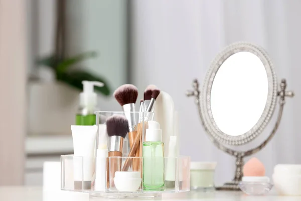 Cosmetic products and makeup accessories on table against blurred background