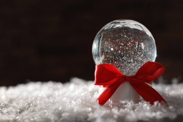 Christmas glass globe with artificial snow on blurred background. Space for text