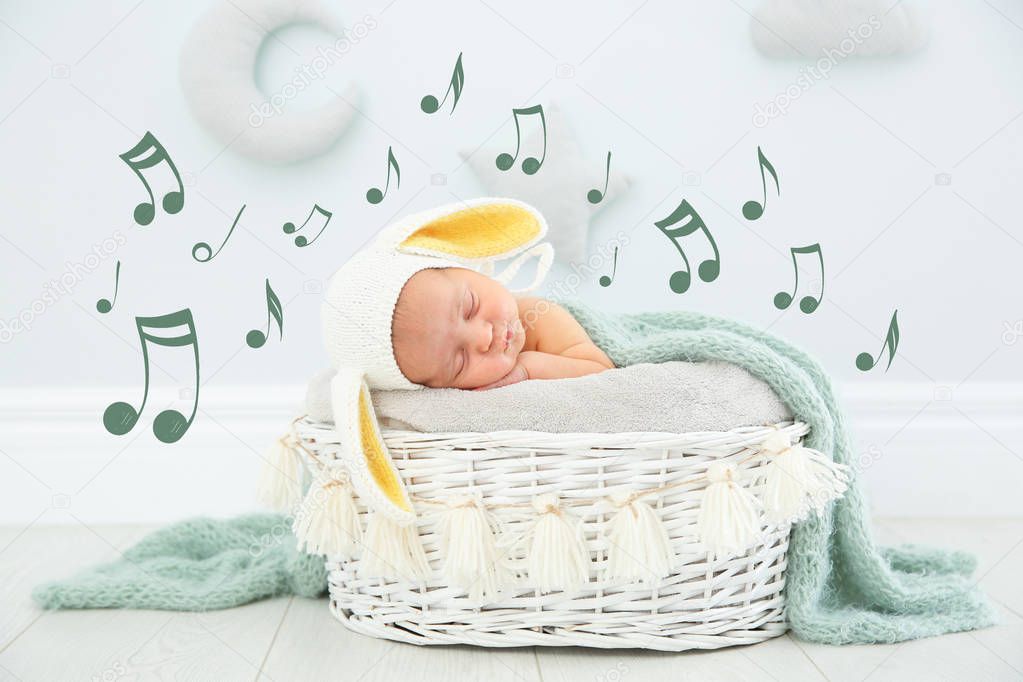 Cute newborn child wearing bunny ears hat sleeping in baby nest and flying music notes indoors. Lullaby song