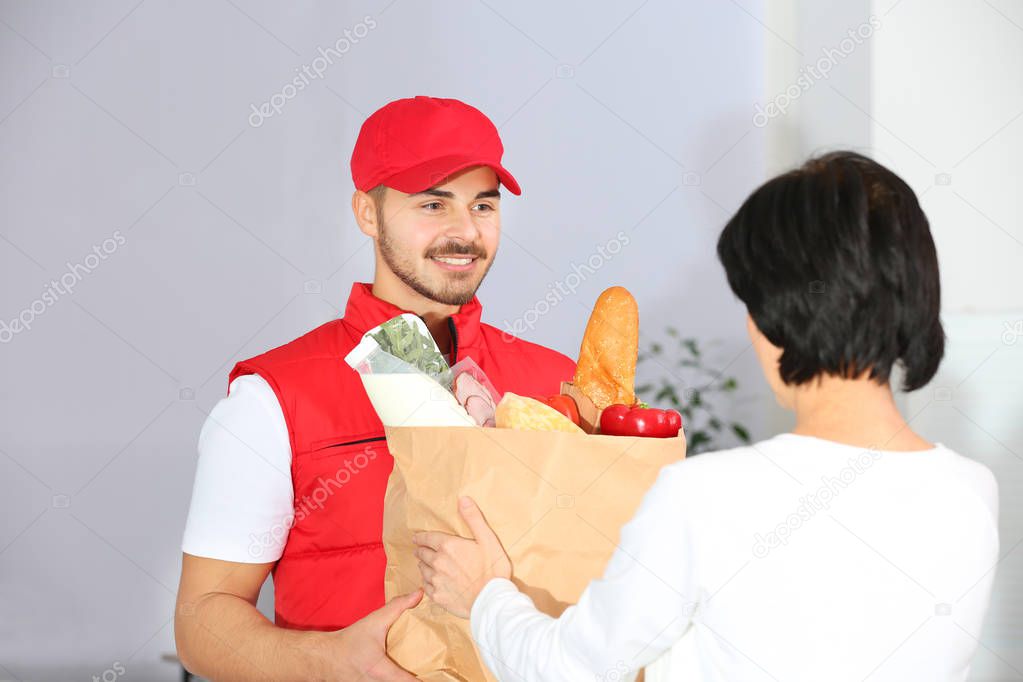 Male courier delivering food to client on light background