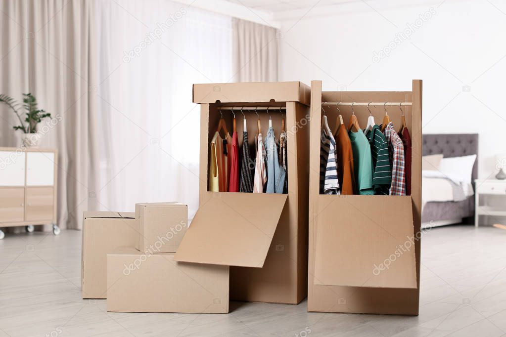 Cardboard wardrobe boxes with clothes on hangers in bedroom. Space for text