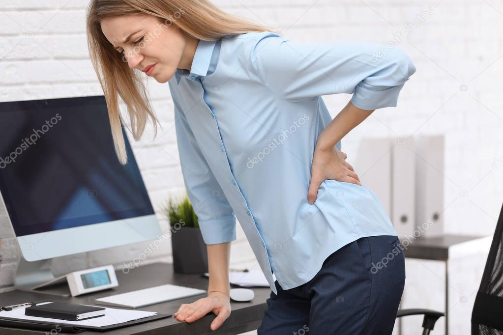 Young woman suffering from back pain in office