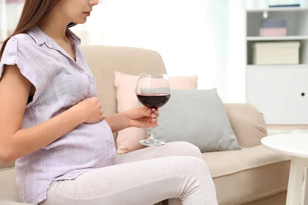 Future mother with glass of wine at home, closeup. Alcohol abuse during pregnancy