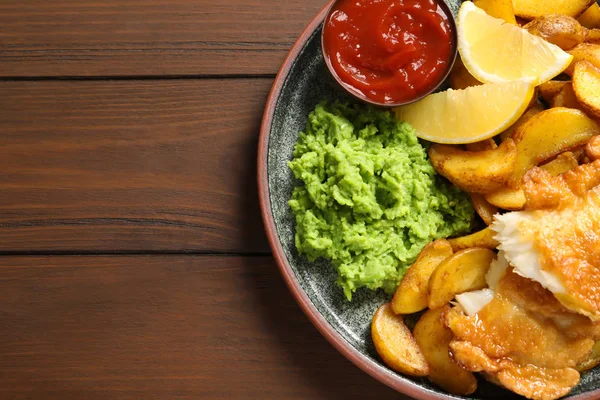 Plate with British traditional fish and potato chips on wooden background, top view. Space for text