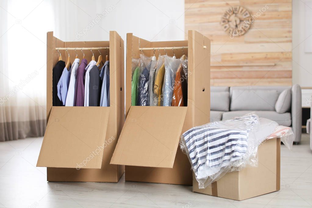 Cardboard wardrobe boxes with clothes on hangers in living room