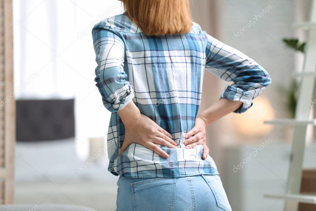 Young woman suffering from back pain at home, closeup
