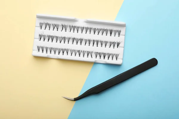 Artificial eyelashes and tweezers on color background, top view