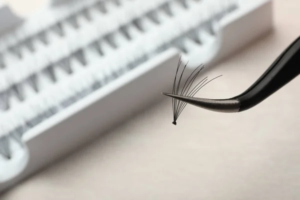 Tweezers with bunch of artificial eyelashes on blurred background, closeup. Space for text