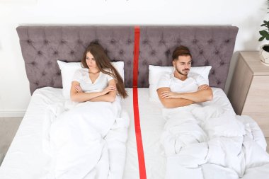 Ayrı ayrı evde yatakta yatan ilişki sorunları olan genç çift üzgün