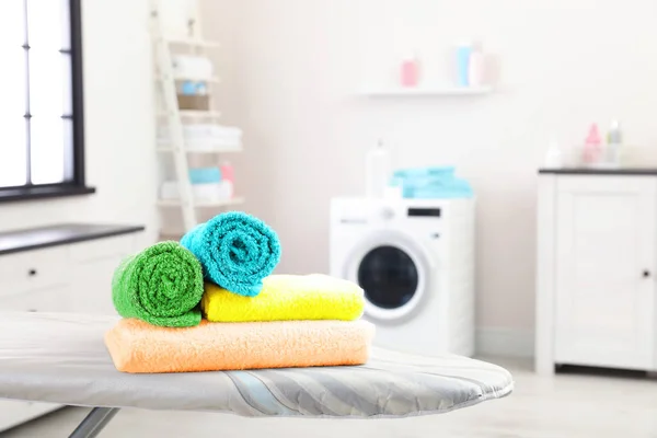 Clean soft towels on ironing board in laundry room, space for text