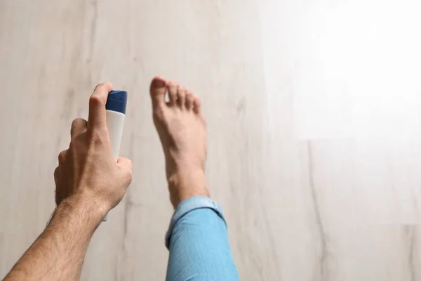 Young man using foot deodorant at home, closeup. Space for text