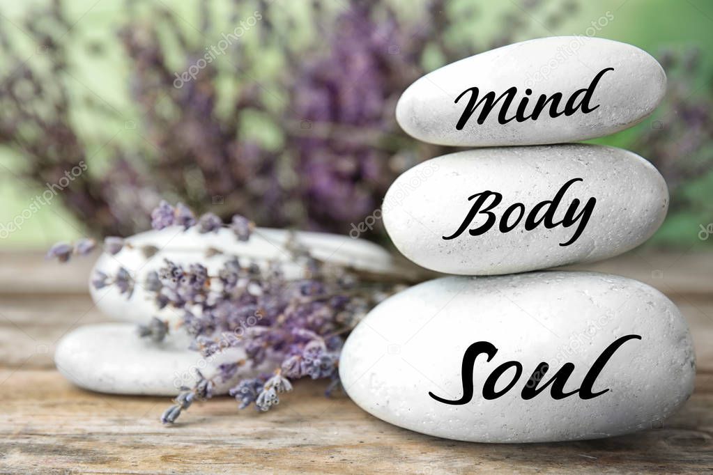 Composition of lavender flowers and zen stones with words Mind, Body, Soul on table against blurred background. Space for text 