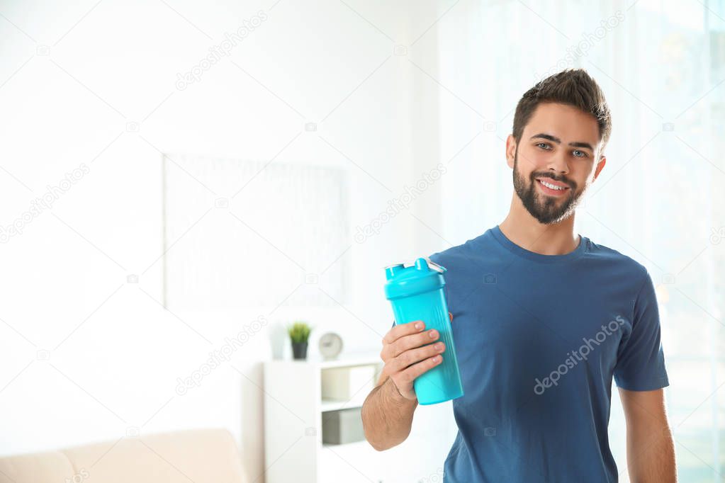 Young man with bottle of protein shake at home. Space for text