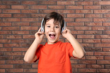 Küçük yakışıklı tuğla duvara kulaklık ile müzik dinlemek