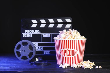 Klaket, reel ve patlamış mısır kova koyu arka plan karşı masada. Sinema izliyor