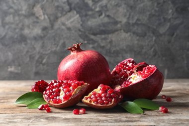 Ripe pomegranates and leaves on table against grey background. Space for text clipart