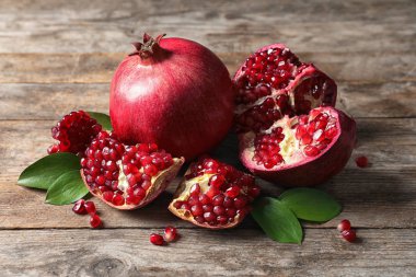 Ripe pomegranates and leaves on wooden background clipart