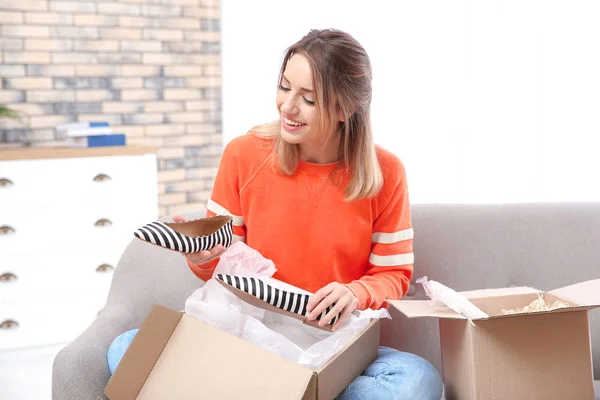 Young woman opening parcel on sofa in living room