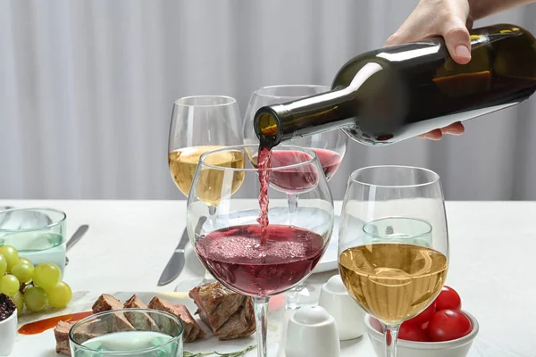 Woman pouring red wine into glass on served table