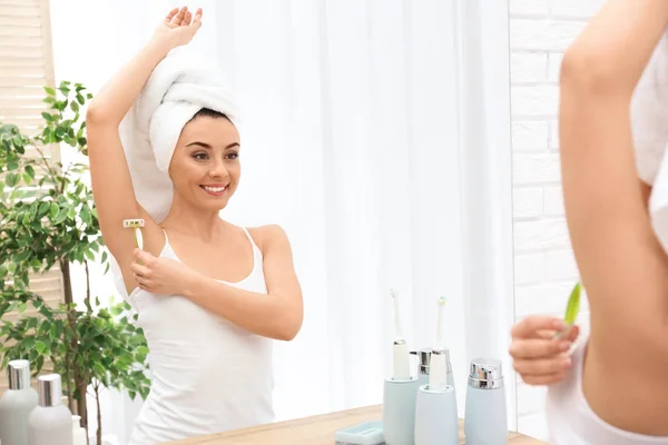 Beautiful young woman shaving armpit at home