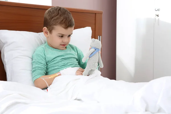 Little child with intravenous drip and toy in hospital bed