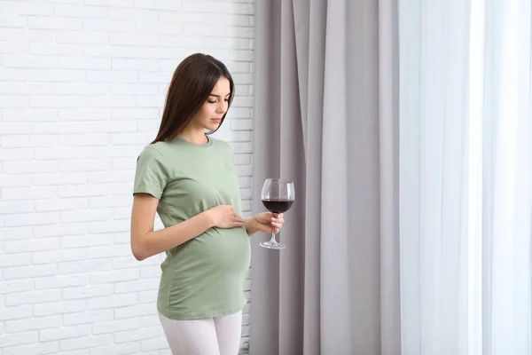 Future mother with glass of wine indoors, space for text. Alcohol abuse during pregnancy