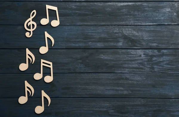 Music notes and treble clef on wooden background, top view. Space for text