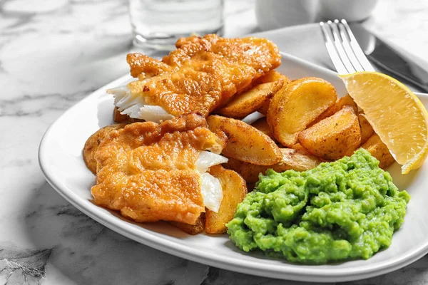 Plate with British traditional fish and potato chips on marble table, closeup