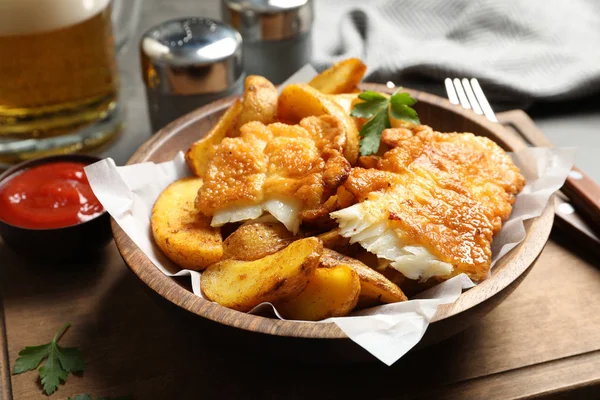 Wooden plate with British traditional fish and potato chips on table