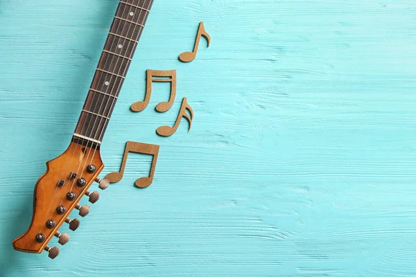 Guitar neck and music notes on wooden background, flat lay. Space for text