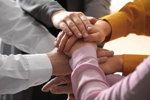 Young people putting their hands together on blurred background, closeup