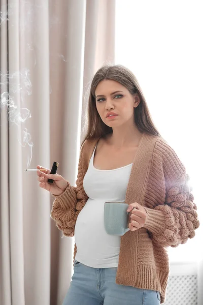 家でタバコを吸ってコーヒーのカップを持つ若い妊婦 胎児に害を与える — ストック写真