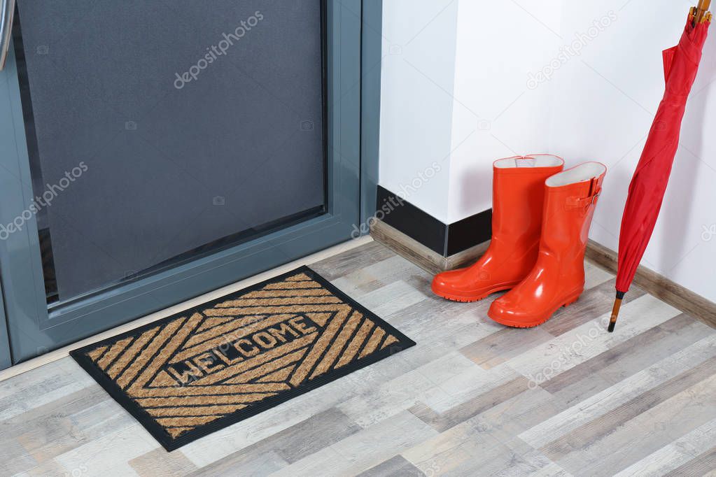 Rubber boots, umbrella and mat near door in hallway