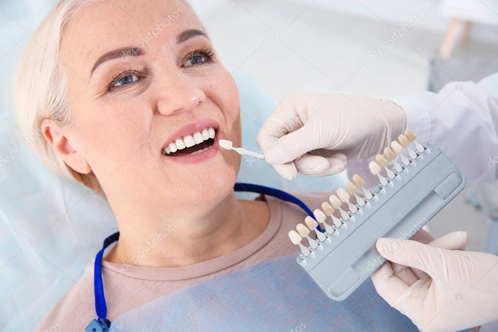 Dentist selecting patient's teeth color with palette in clinic