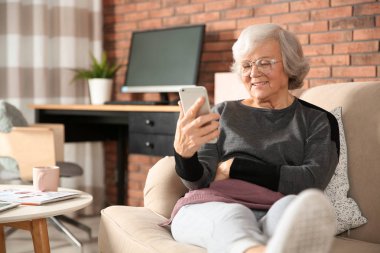 Yaşlı kadın kanepe oturma odasında Smartphone kullanarak