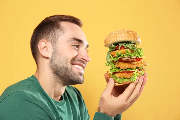 背景色で巨大なハンバーガーを食べる若い飢えた男 — ストック写真