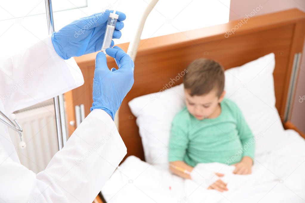 Doctor adjusting intravenous drip for little child in hospital, closeup