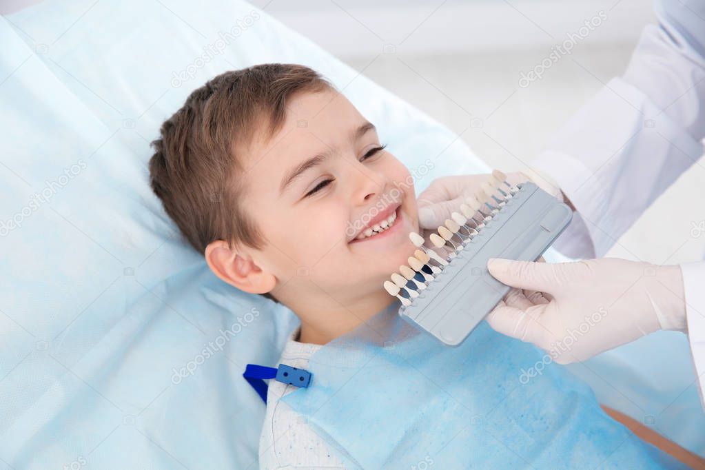 Dentist selecting cute boy's teeth color with palette in clinic