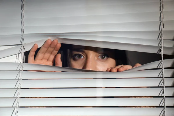 Curious woman looking through Venetian window blinds