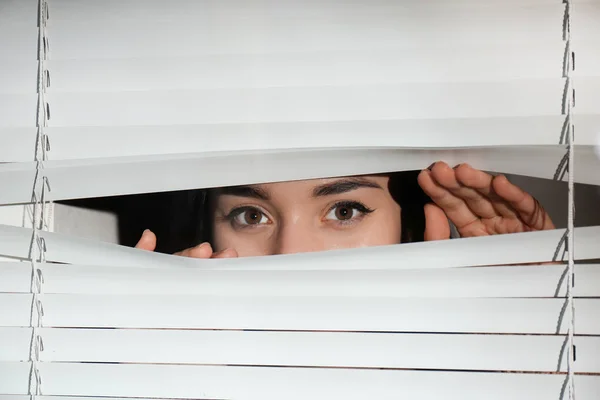 Curious woman looking through Venetian window blinds