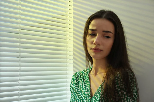 Young woman near window with Venetian blinds. Space for text